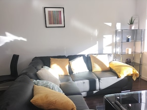 En moderne stue med en hjørnesofa, et glasbord og et indrammet kunstværk på væggen.