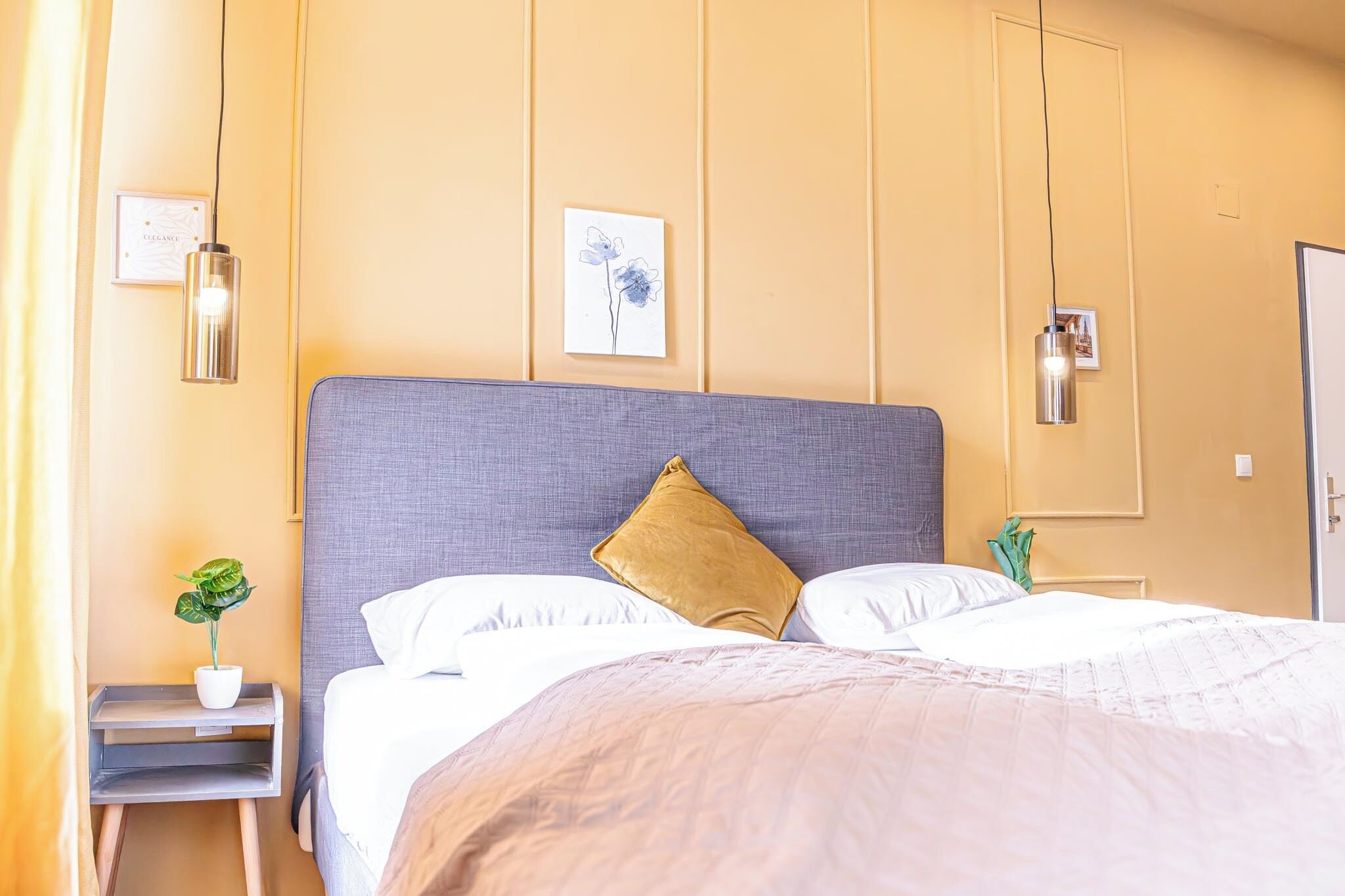 Une chambre d’hôtel avec un grand lit, une table de chevet ornée d’une plante et un tableau accroché au mur.