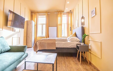 A modern hotel room with a bed, a sofa, a TV, and a small table.