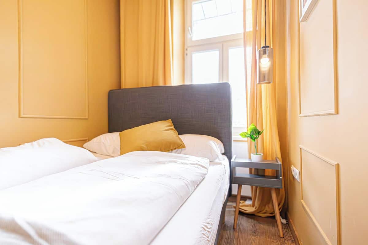A hotel room with a bed, a nightstand, a lamp, and a window with curtains.