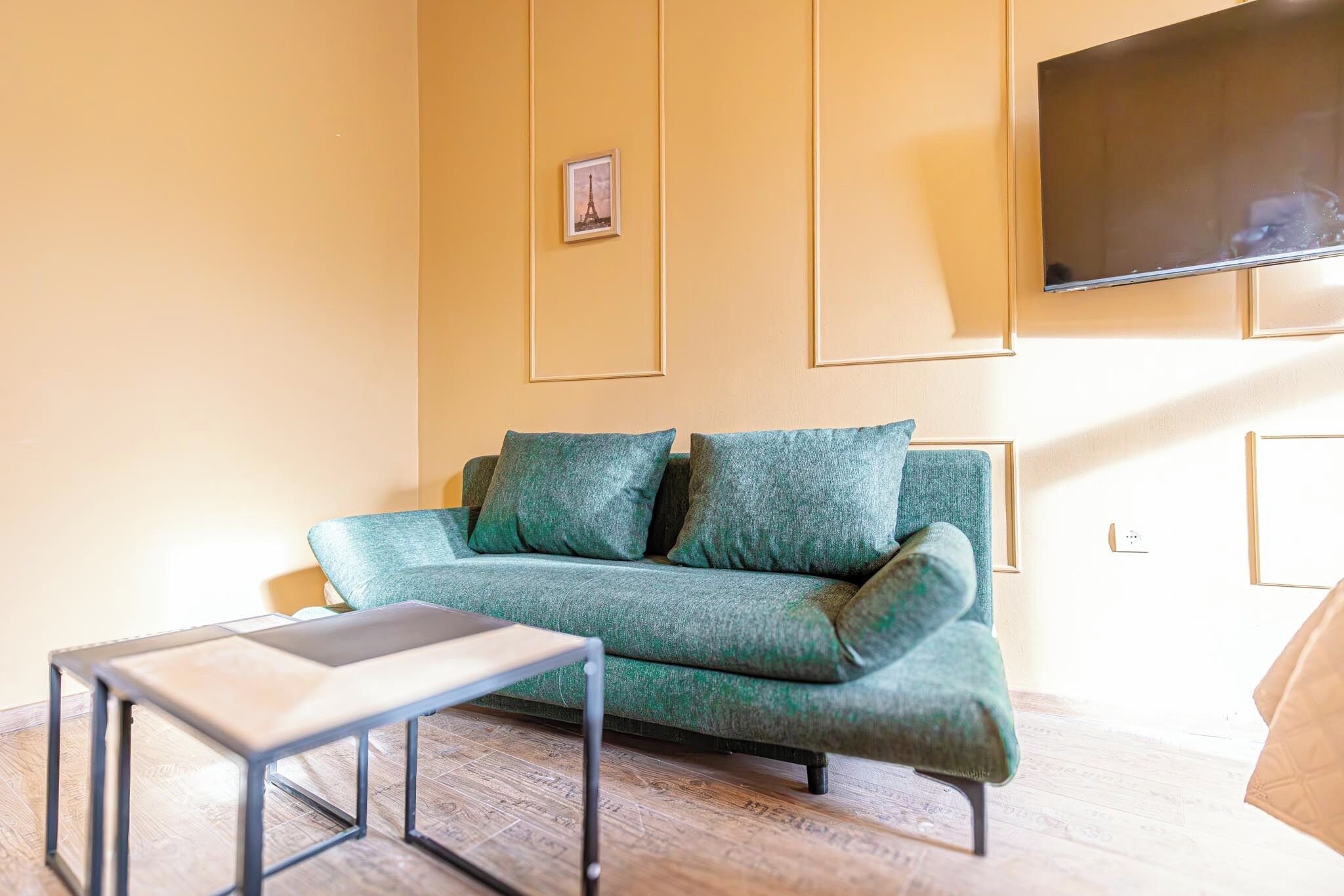 Un salon moderne avec un canapé vert, une petite table et un téléviseur à écran plat fixé au mur.