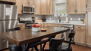 A modern kitchen with wooden cabinets, stainless steel appliances, and a dining area with a wooden table and chairs. - Sunrise Mountain Escape - Modern 1 Bed, 1 Bath - Gorgeous Views Near BRPW & I-77 (Fancy Gap)