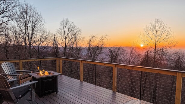 A wooden deck with a fire pit and seating, overlooking a forested landscape during sunset. - Sunrise Mountain Escape - Modern 1 Bed, 1 Bath - Gorgeous Views Near BRPW & I-77 (Fancy Gap)