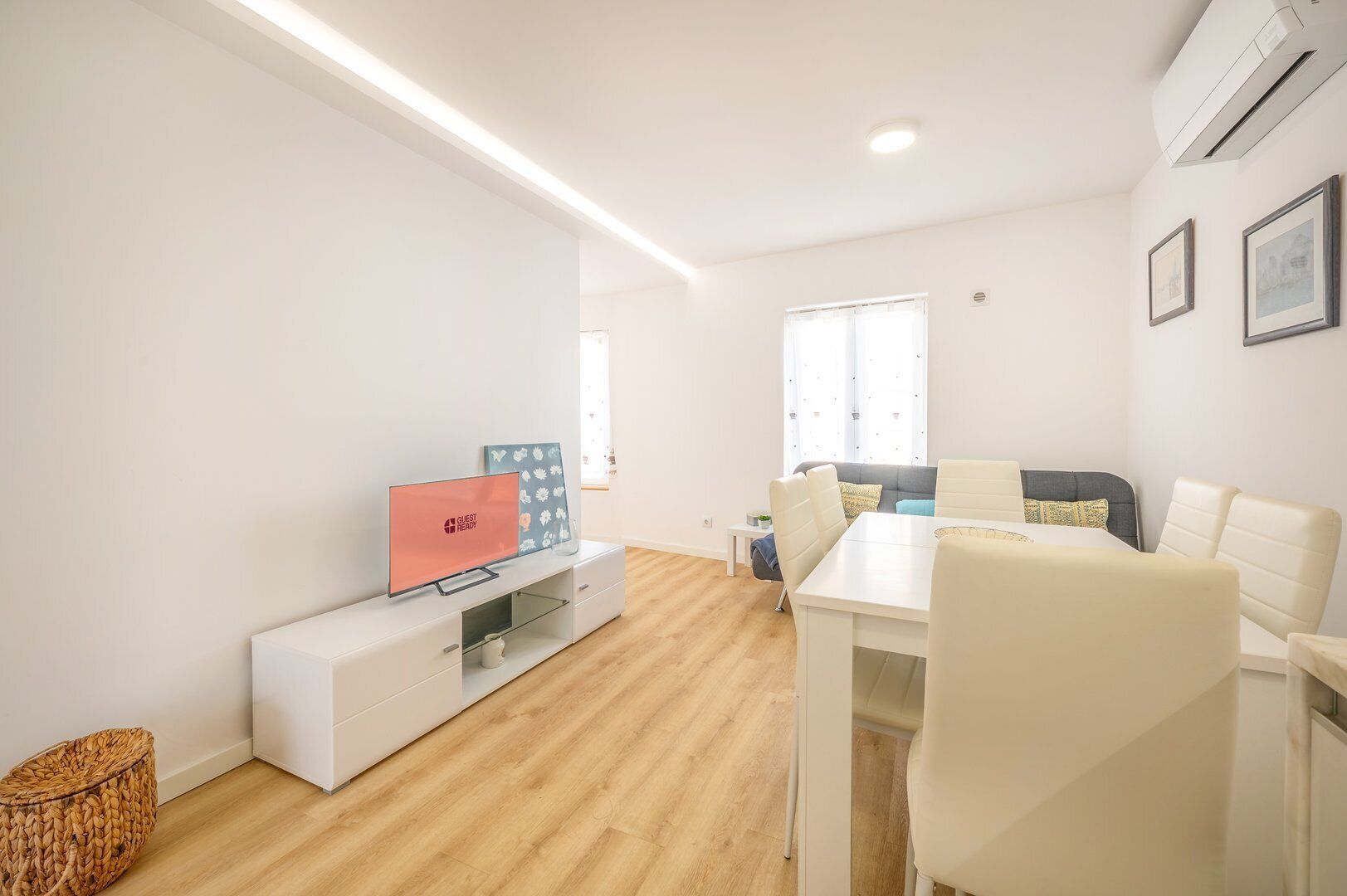 Una sala moderna con un televisor de pantalla plana, una mesa de comedor con sillas, un sofá y una pequeña mesita auxiliar.