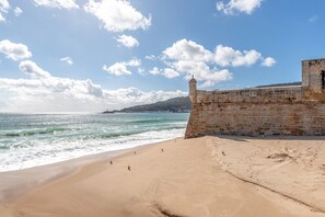 A beach with a stone wall and a lighthouse in the background.