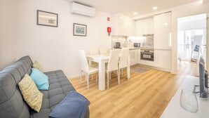 Un apartamento moderno con un sofá gris, una mesa de comedor blanca y una zona de cocina.