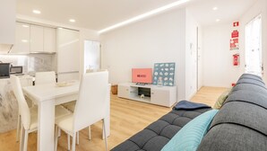 Una sala de estar moderna con un sofá, una mesa de comedor con sillas, un televisor y una cocina con armarios y un microondas.