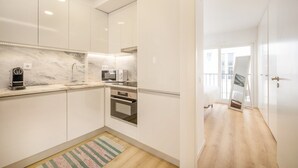 Una cocina moderna con armarios blancos, salpicadero de mármol, horno empotrado y cafetera.