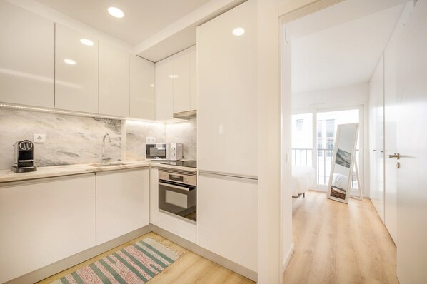 A modern kitchen with white cabinets, a marble backsplash, a built-in oven, and a coffee maker.