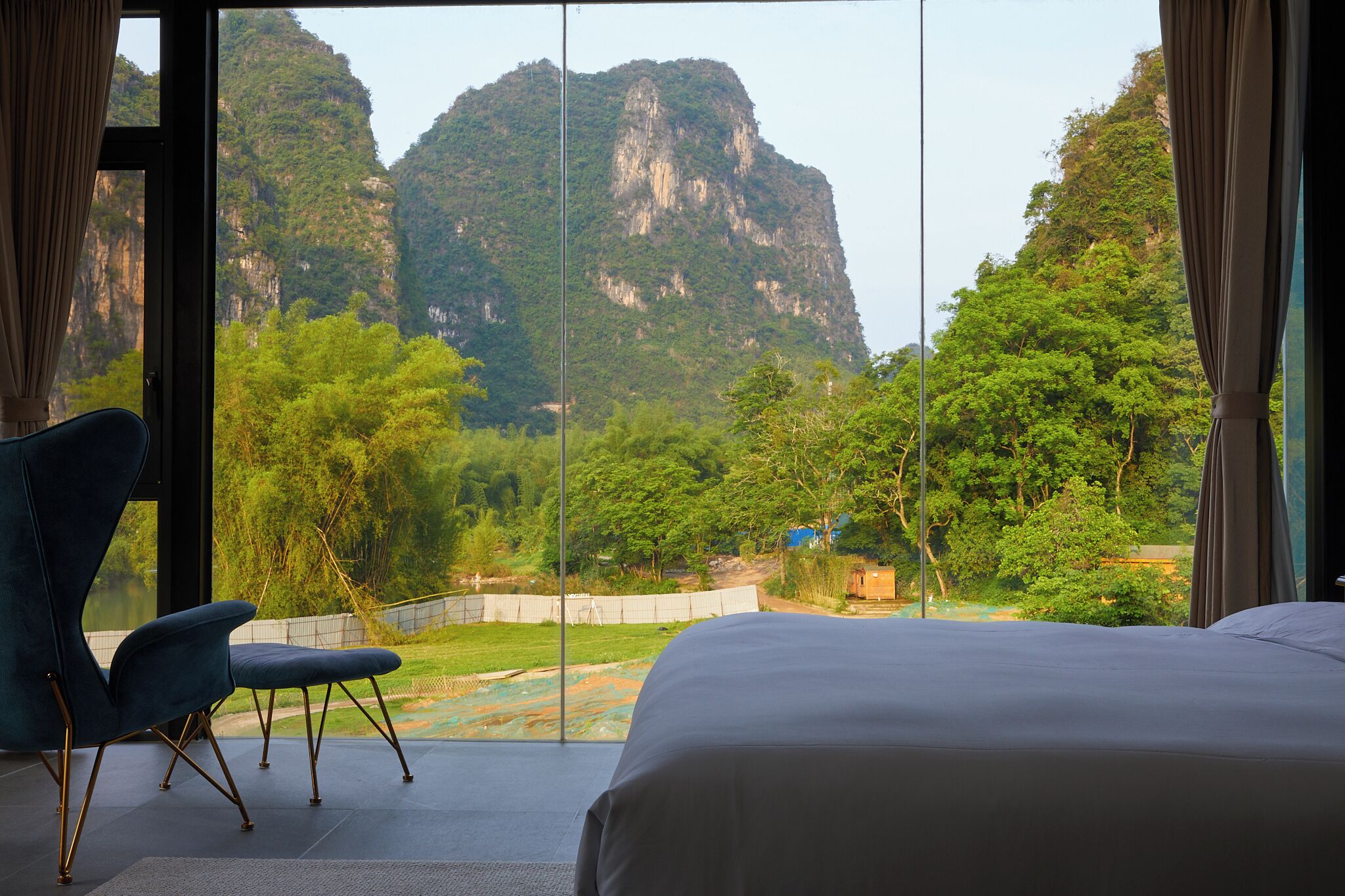 A hotel room with a large window offering a view of a mountainous landscape and a river.