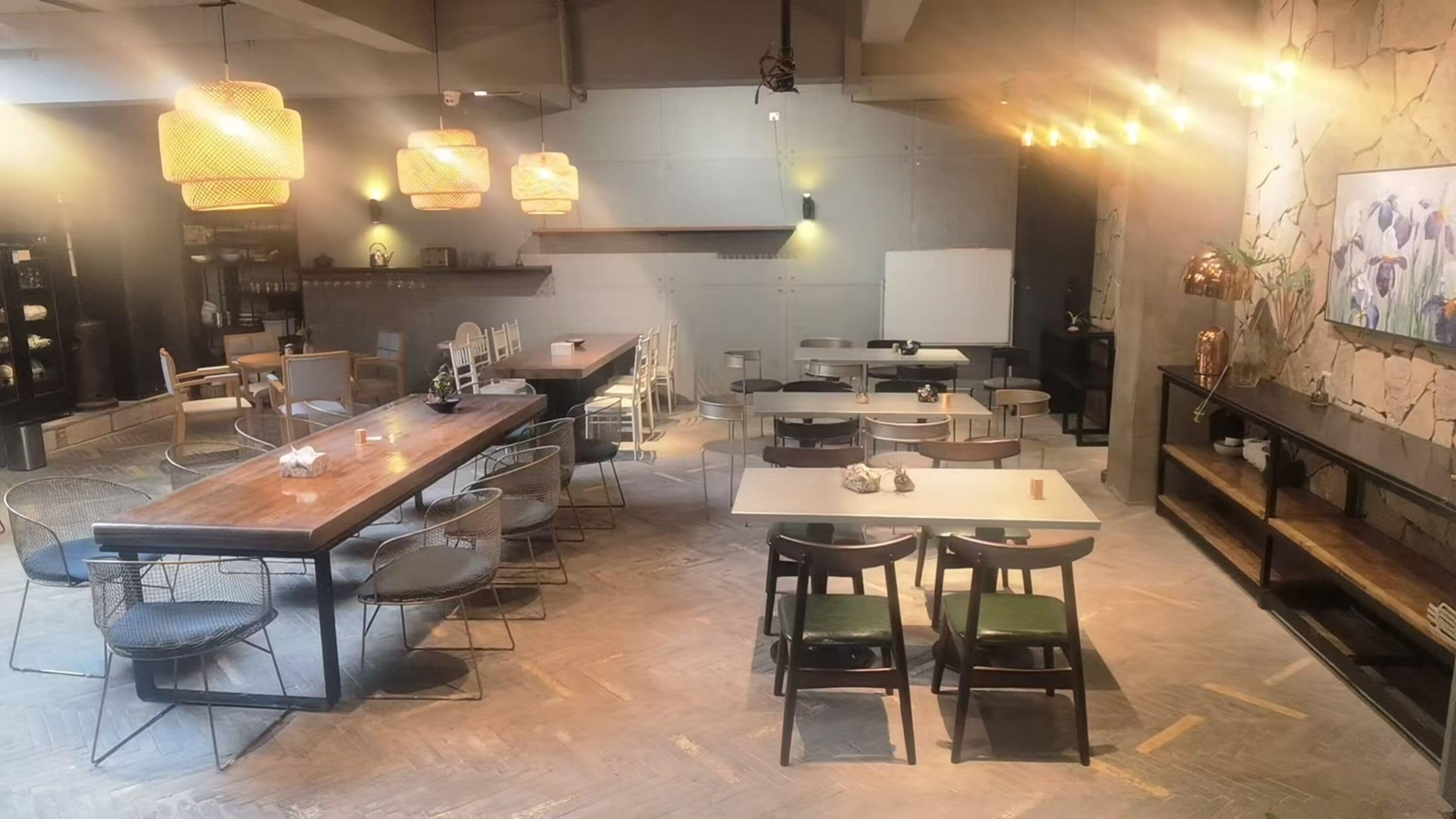 A modern restaurant with a long communal table, smaller tables, and chairs.