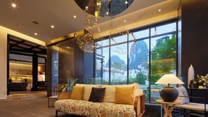 A modern living room with a sofa, a lamp, and a large window with a view of the outdoors. - Yangshuo The One Hotel (Guilin)