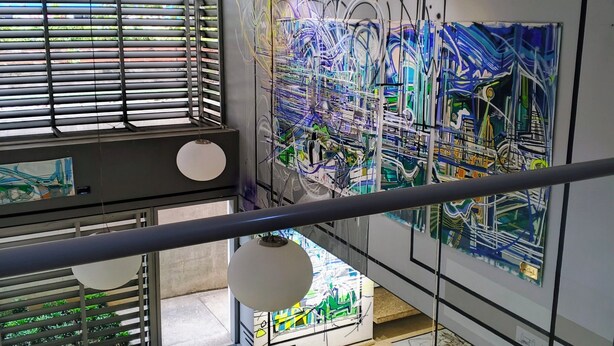 Eine moderne Kunstgalerie mit abstrakten Gemälden, einer Treppe und Blick ins Grüne.