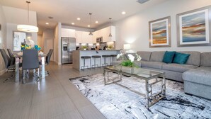 Un salon moderne avec une table basse en verre, un canapé gris et un coin repas comprenant une table et des chaises blanches.