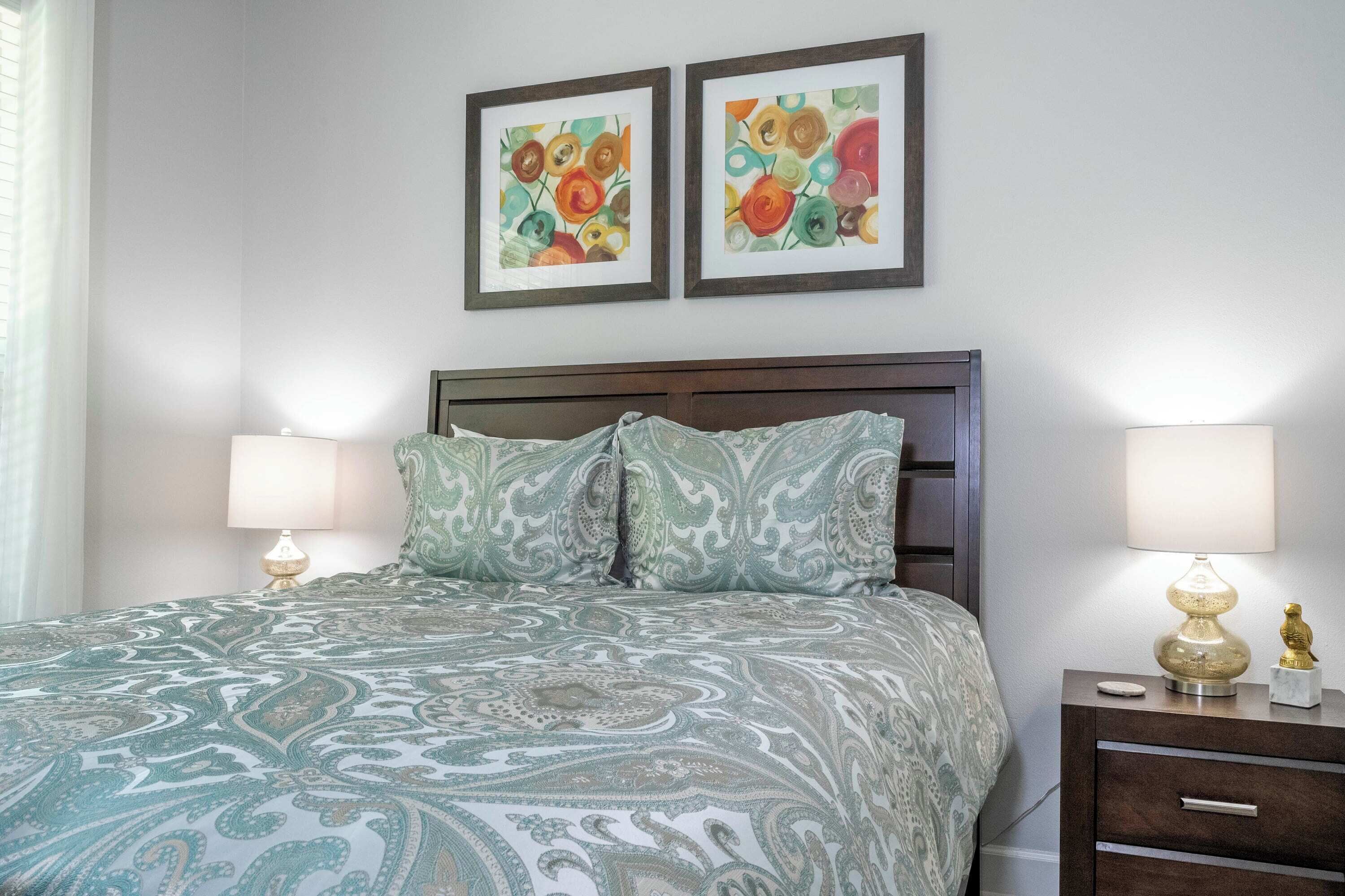 A neatly made bed with patterned bedding, a wooden headboard, two bedside lamps, and a nightstand with a decorative item.