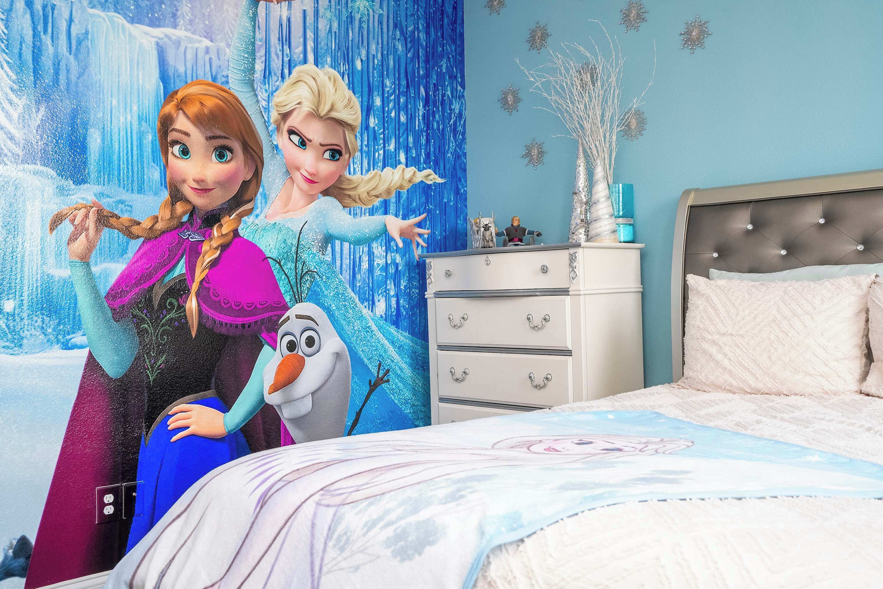 A bedroom with a bed, dresser, and a wall with a Frozen-themed mural.