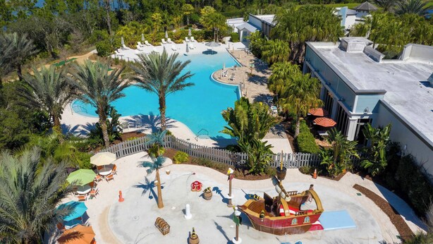 Un resort con una grande piscina, palme e un'area giochi con una nave pirata.