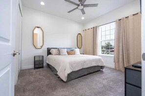Une chambre à coucher avec un lit, un ventilateur de plafond, une fenêtre avec des rideaux et une table de chevet.