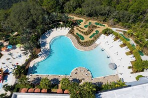 Vue aérienne d’un complexe hôtelier doté d’une grande piscine, de chaises longues et d’un espace paysager agrémenté de sentiers.
