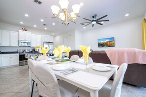 Une cuisine moderne avec des meubles blancs, un coin repas avec une table dressée pour deux personnes et un ventilateur de plafond.
