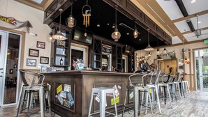 Angolo bar con un bancone in legno, sgabelli metallici e lampade pendenti.
