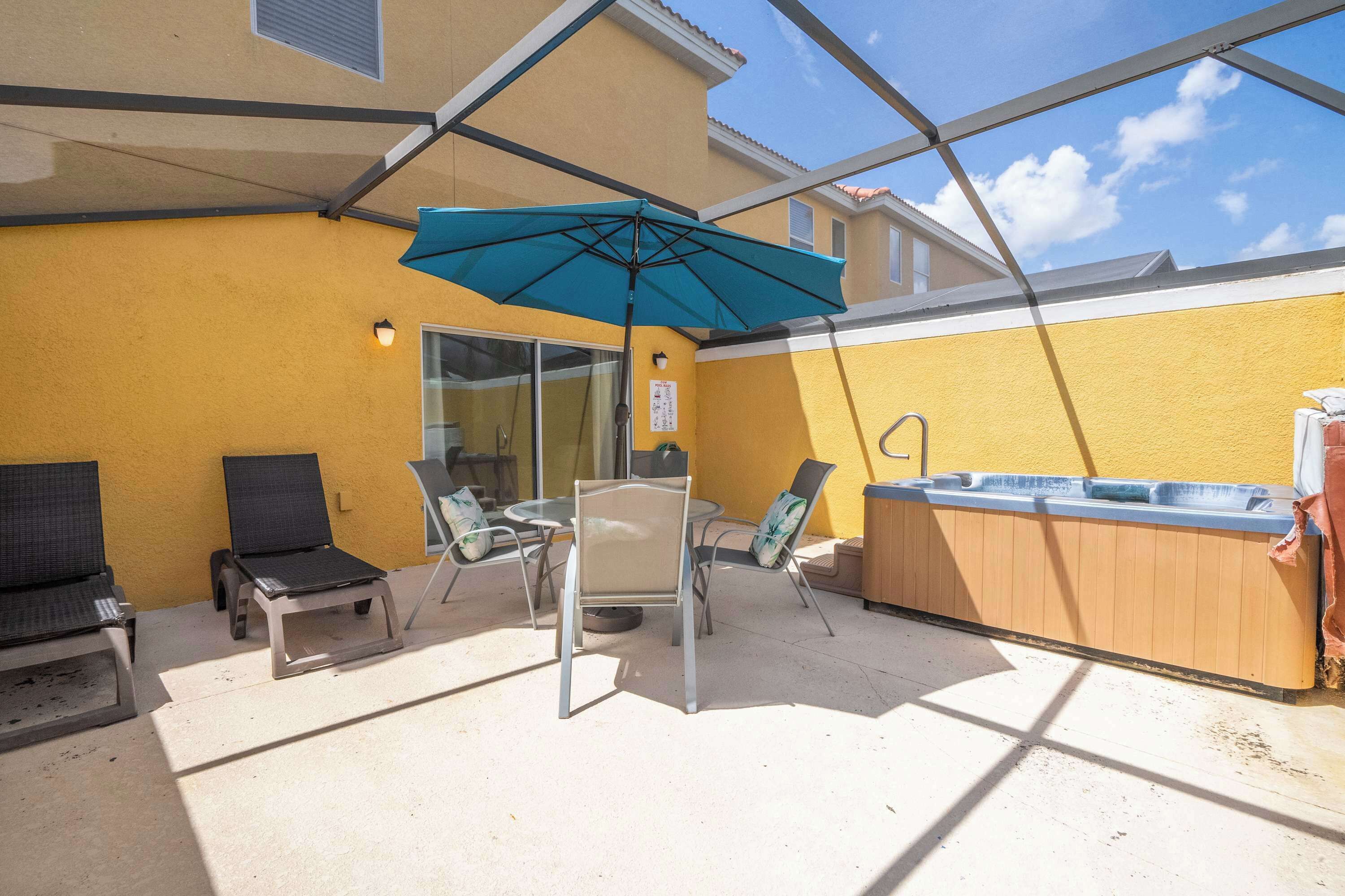 A patio with a table and chairs, a hot tub, and a blue umbrella.