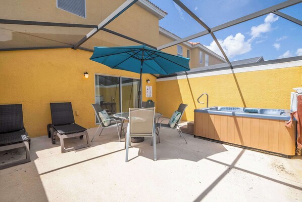 Une terrasse avec une table et des chaises, un jacuzzi et un parasol bleu.
