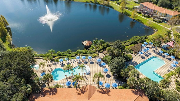 An aerial view of a resort with a large central lake, a fountain, and multiple swimming pools surrounded by palm trees and lounge areas. - Cozy 2Bd Spa/Jacuzzi Close To Disney @ Encantada 3029 (Kissimmee)
