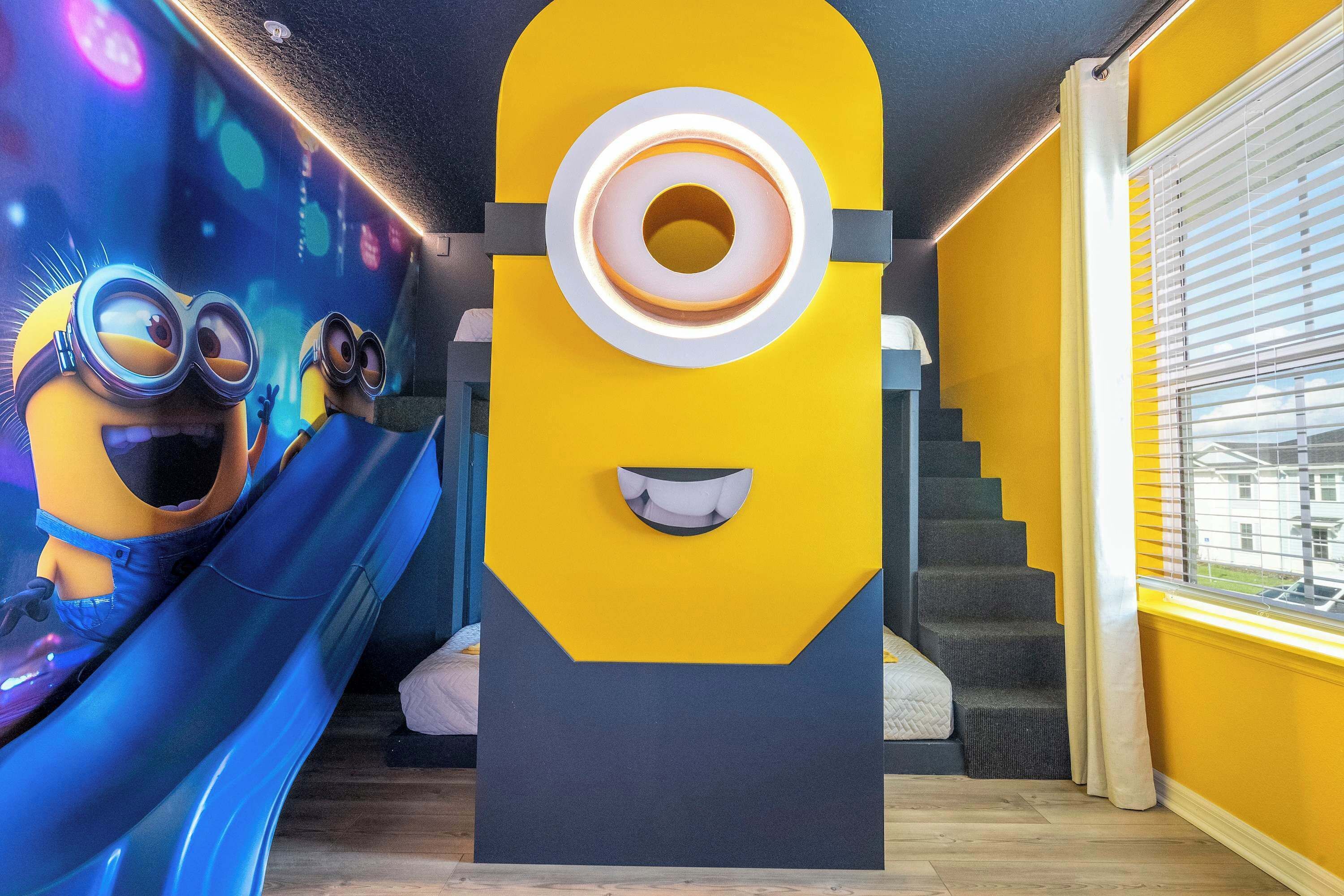 A room with a large Minion sculpture, a blue slide, and a staircase.