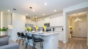 A modern kitchen with white cabinets, a central island with bar stools, and pendant lighting. - Fabulous 5Bd Pool & Game Room @ Windsor Cay 1253 (Clermont)
