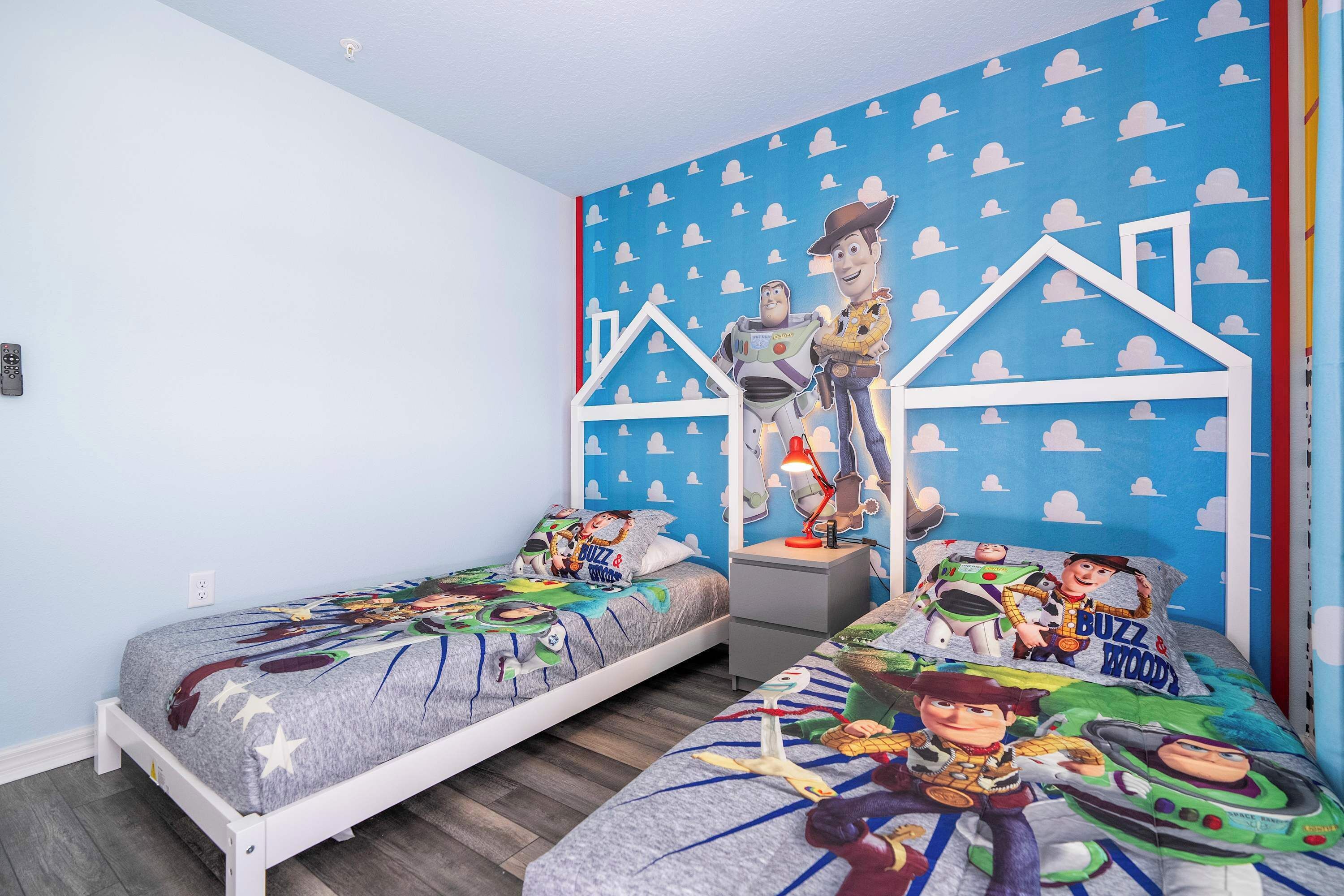 A bedroom with two beds, each adorned with Buzz Lightyear and Woody-themed bedding.