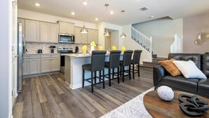 A modern kitchen with a central island, bar stools, and pendant lighting.