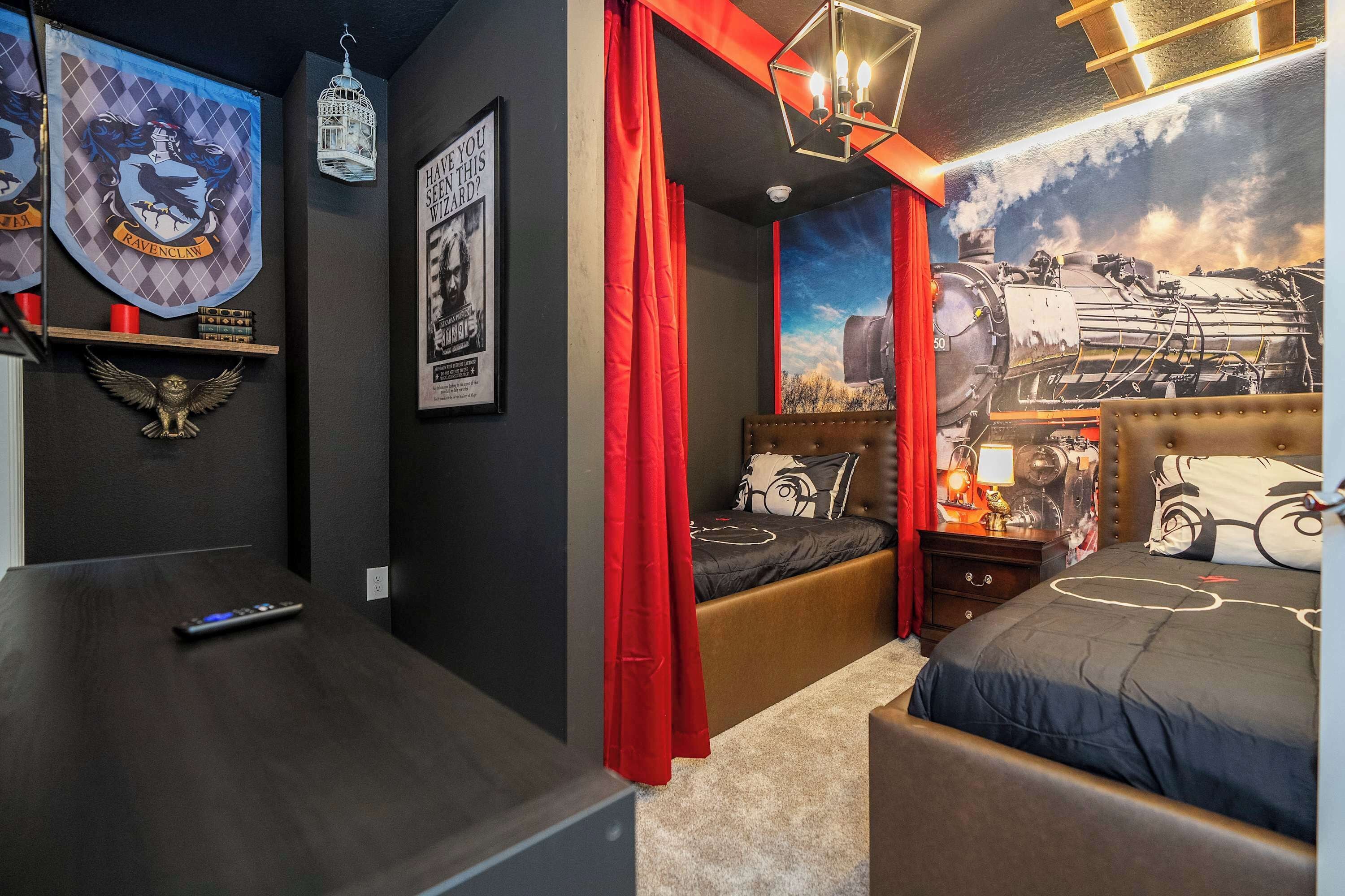 Une chambre à coucher avec un lit, une table de chevet, un rideau rouge et un mur orné d’une affiche.