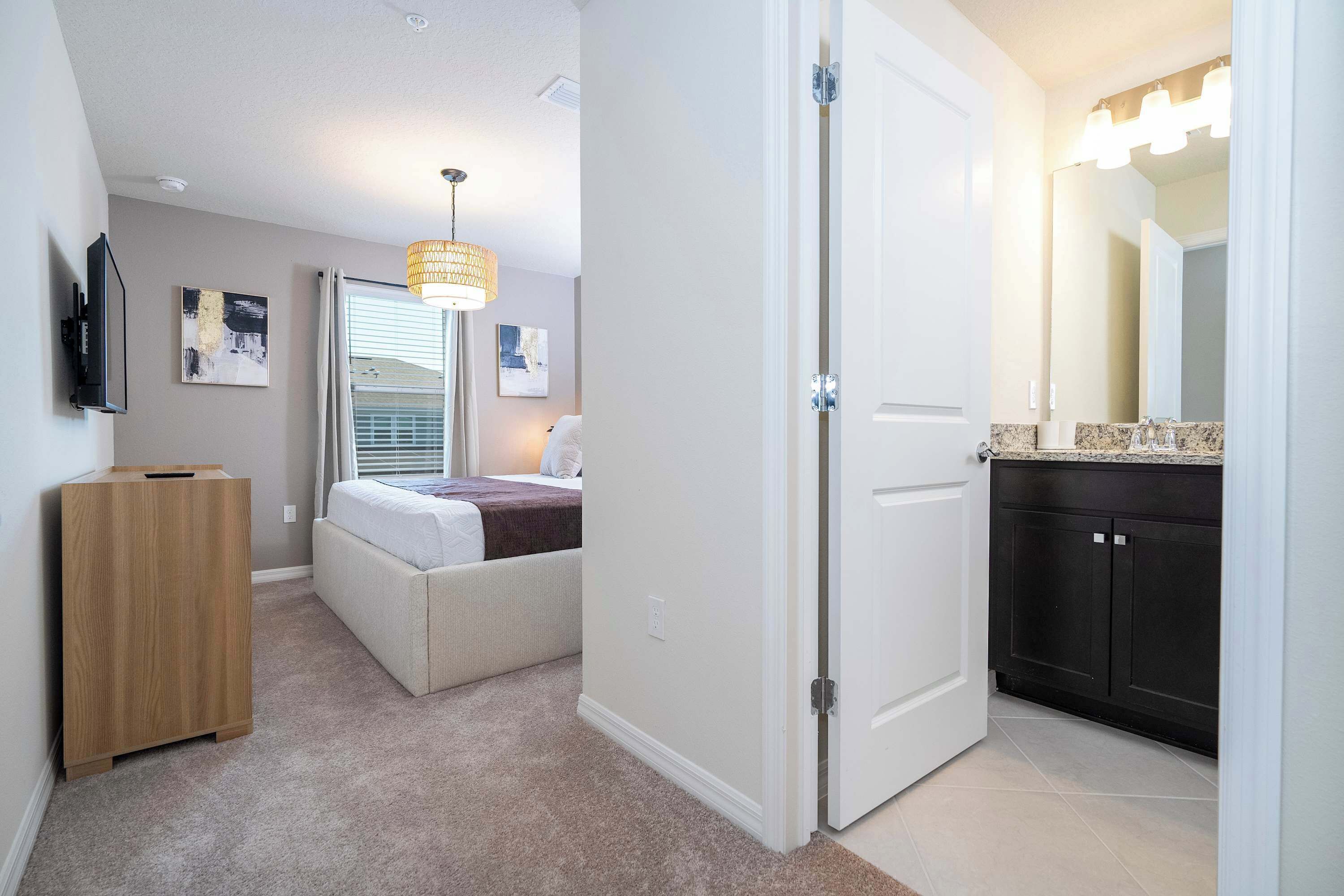A bedroom with a bed, a bedside table, a lamp, a TV, and a window with blinds.