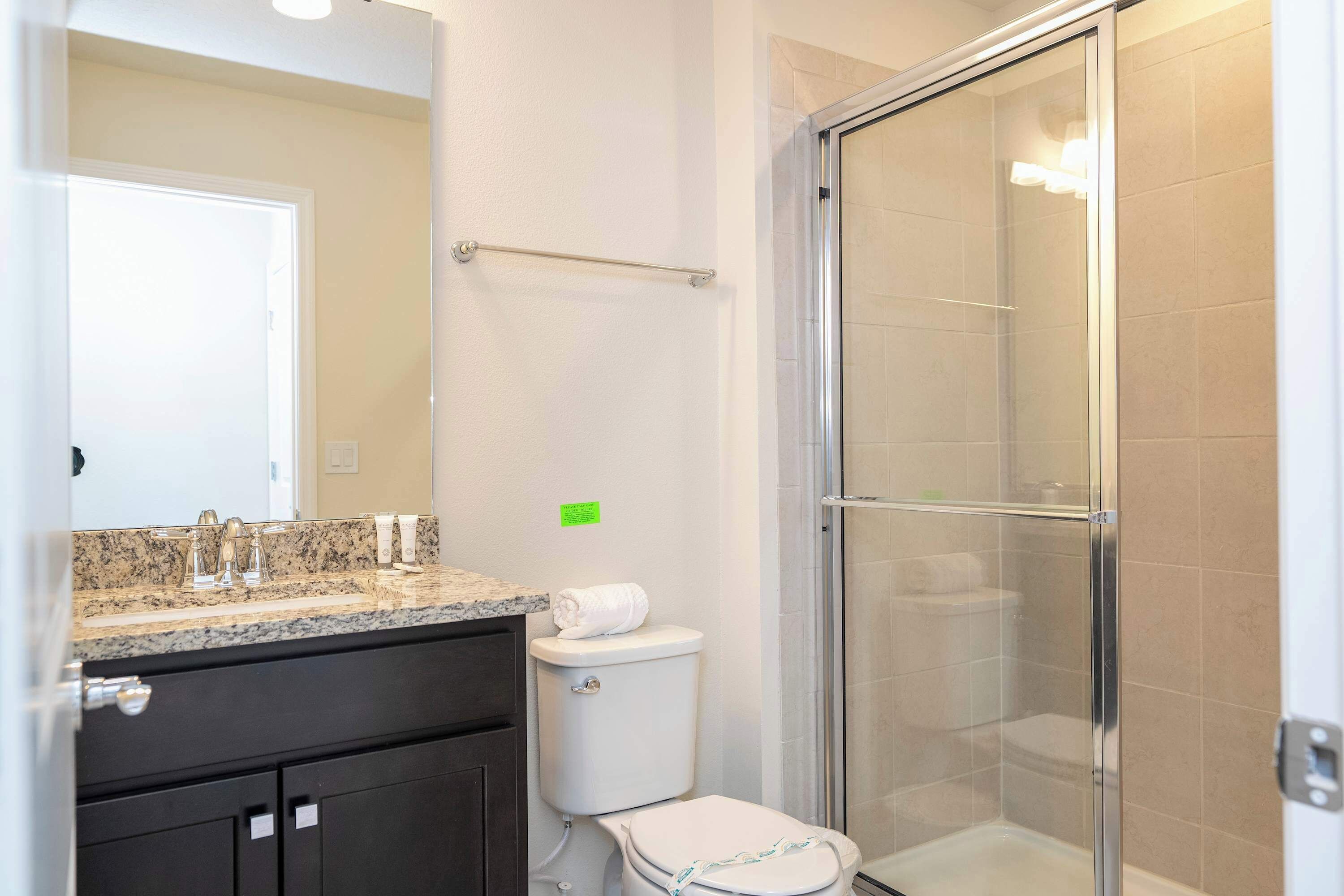 A bathroom with a glass-enclosed shower, a sink with a granite countertop, and a toilet.