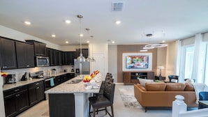 A modern kitchen with dark cabinets, a central island, and a dining area with a brown leather sofa.