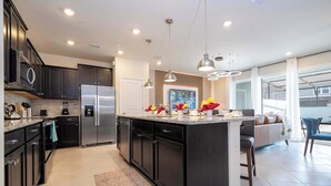 A modern kitchen with dark cabinetry, stainless steel appliances, and pendant lighting.