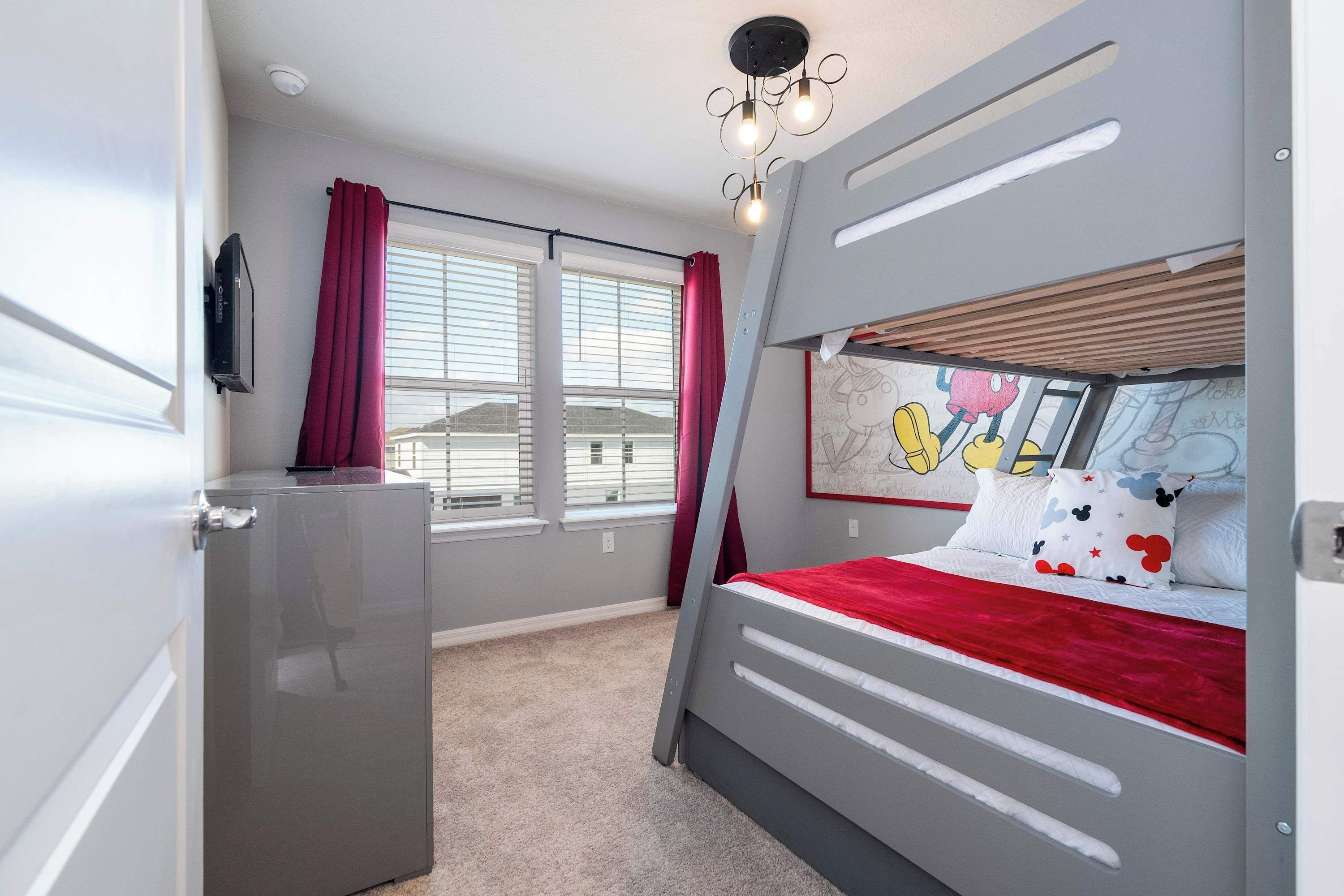 Un dormitorio con literas, un refrigerador pequeño, una ventana con persianas y una lámpara en el techo.