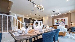 A modern dining area with a wooden table set for four, blue upholstered chairs, and a staircase leading to an upper level.