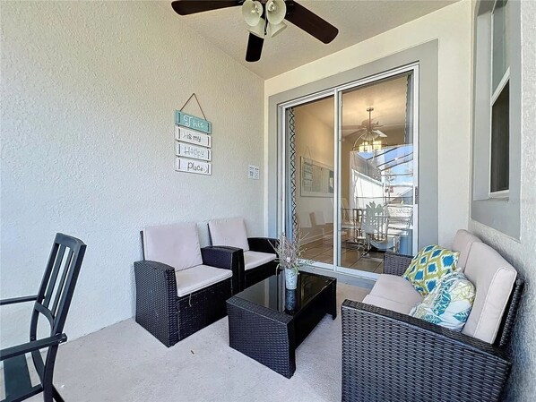 Un'area patio con mobili in vimini, un tavolo in vetro e una ventola a soffitto.