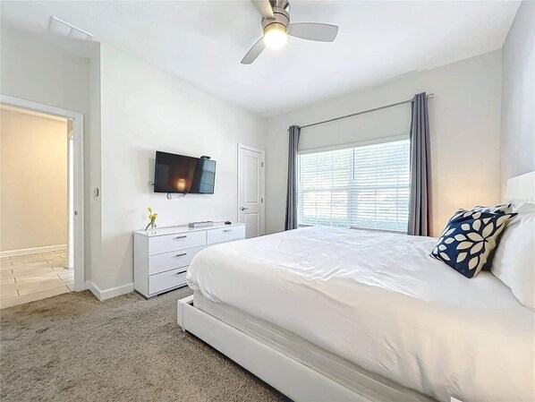 A bedroom with a bed, a TV, a dresser, and a window with curtains. - Stunning 4Bd W/ Pool @ Storey Lake 5019 (Kissimmee)
