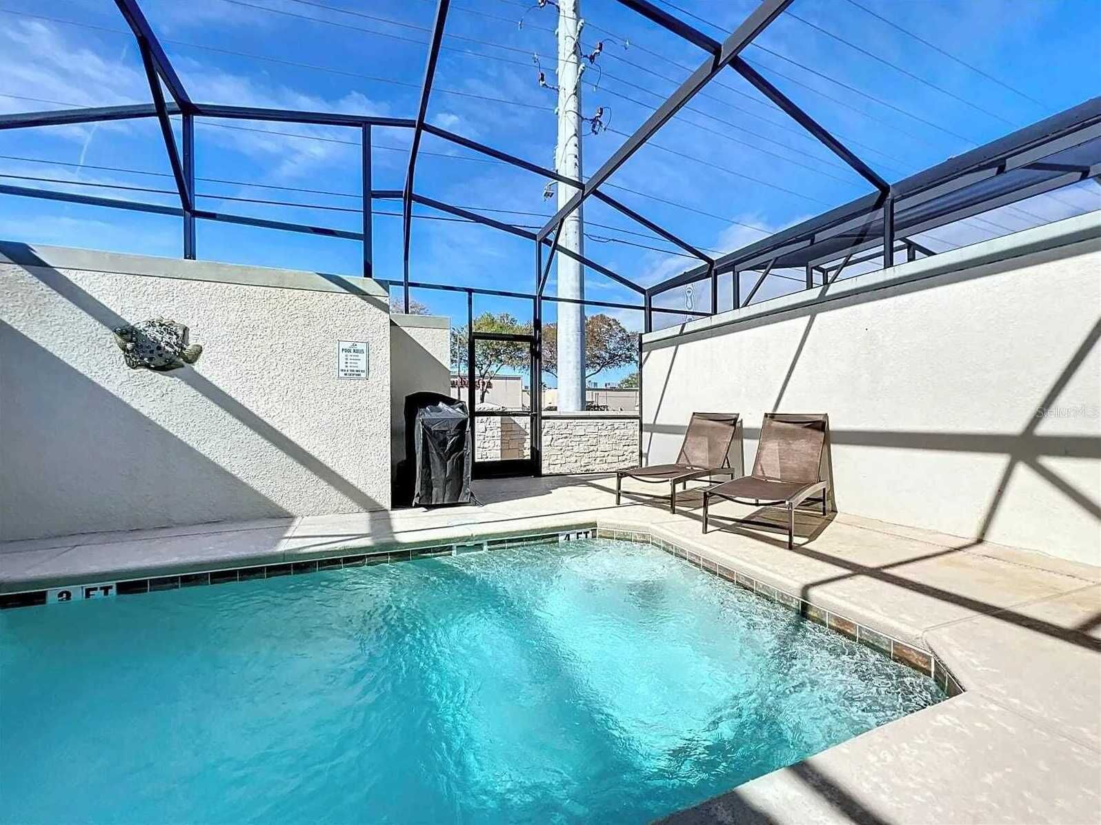 An indoor swimming pool with a glass ceiling, a small door, and two lounge chairs.