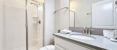 Et moderne badeværelse med bruseniche, toilet, vask med spejl og et badeværelsesmøbel med skabe.