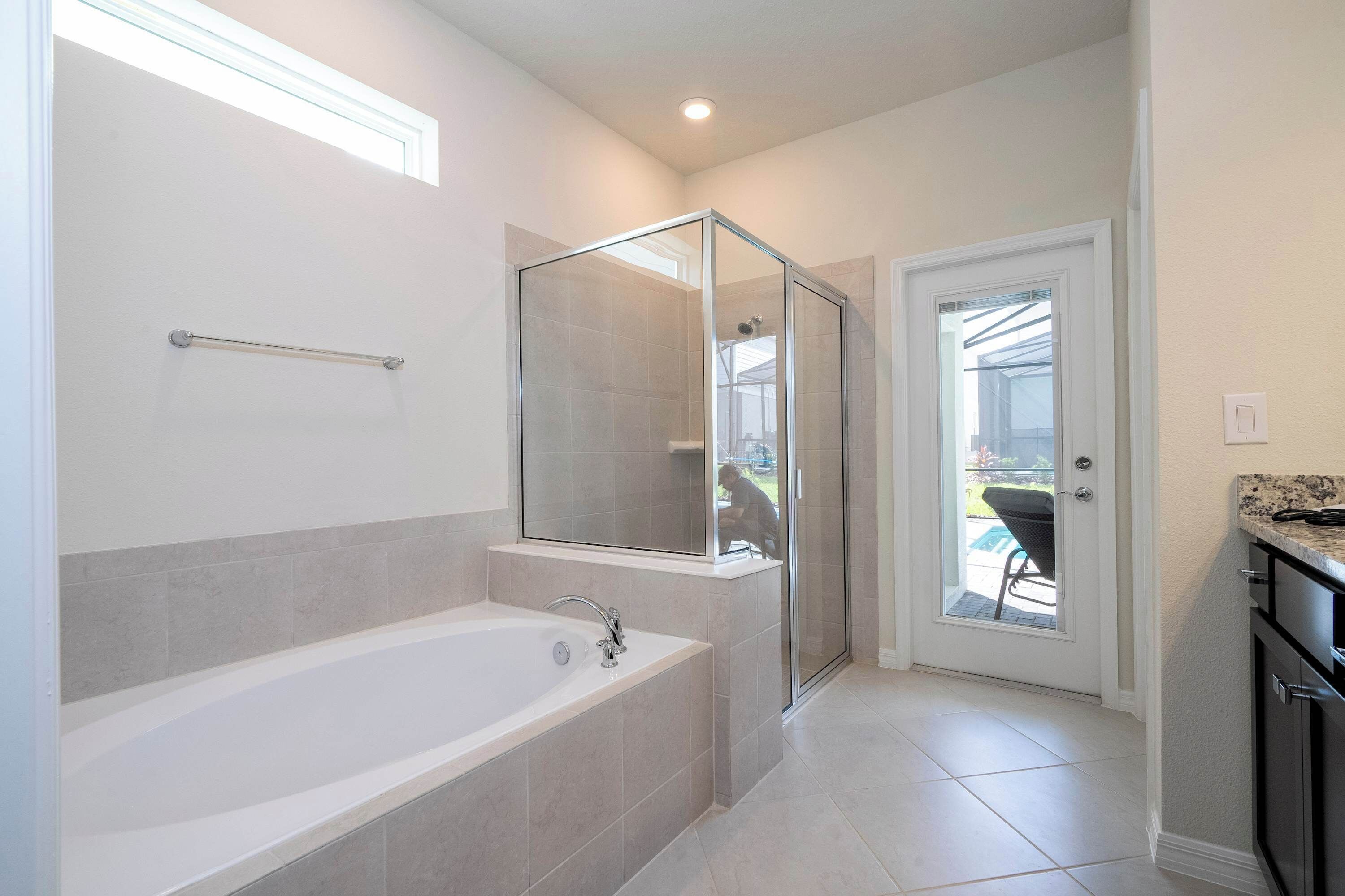A modern bathroom with a large bathtub, a glass shower enclosure, and a view of the outdoors through a door.