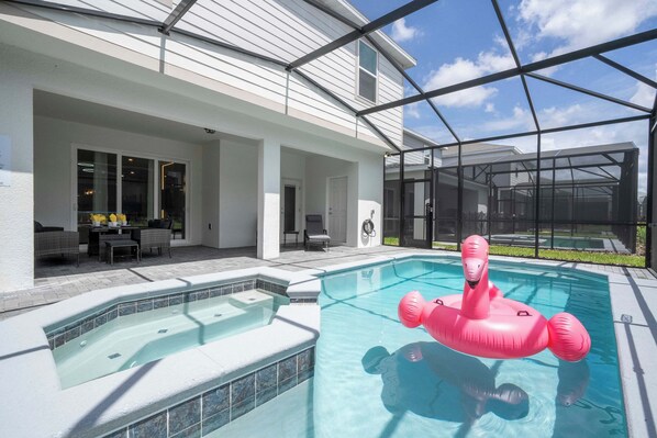 Une piscine avec un jacuzzi, un patio couvert et une vue sur une maison.