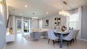 Ett modernt matområde med ett runt bord, grått klädda stolar och en kristallkrona.