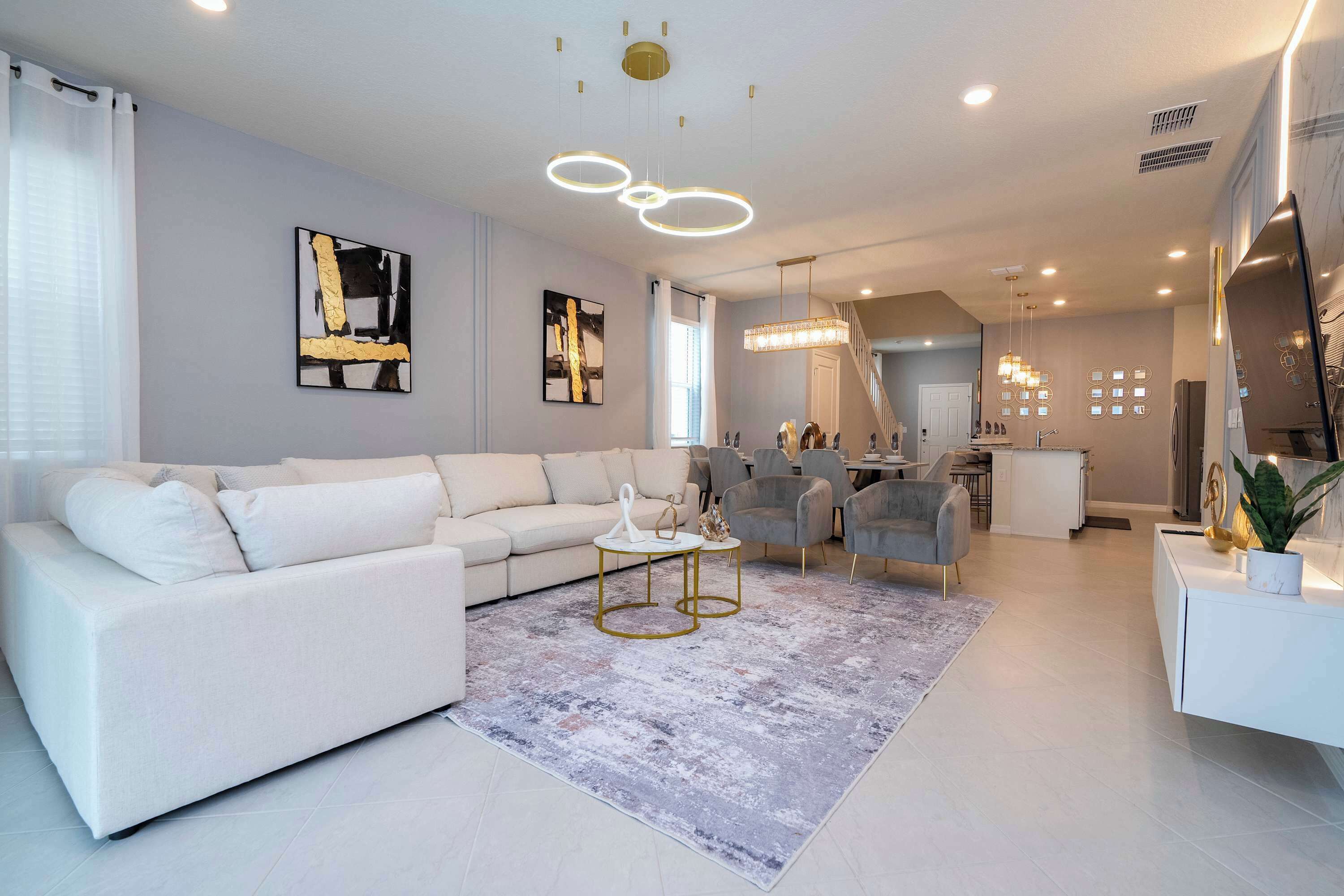 A modern living room with a white sectional sofa, a grey rug, and a dining area with grey chairs.