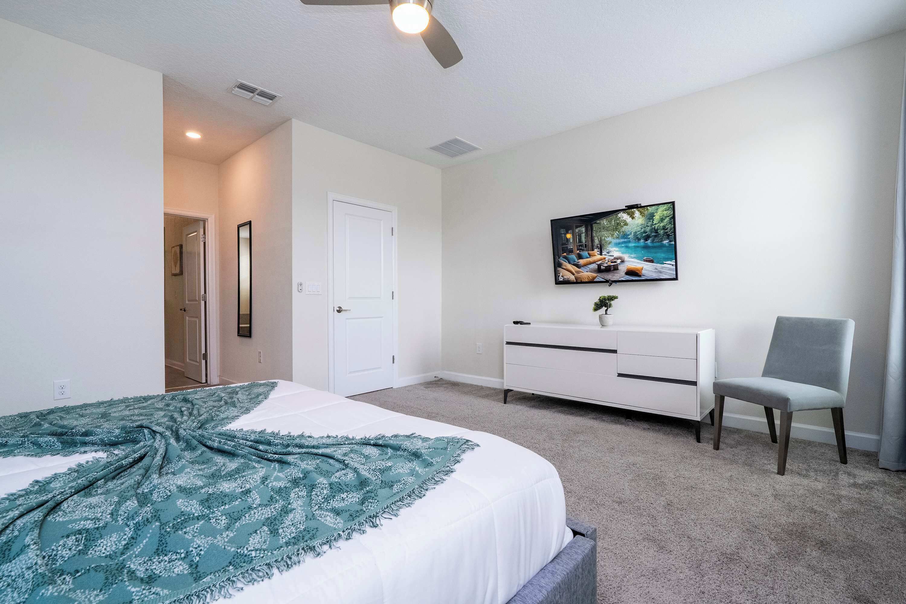 A bedroom with a bed, a dresser, a chair, and a TV on the wall.