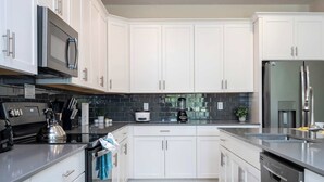 A modern kitchen with white cabinets, stainless steel appliances, and a black tiled backsplash. - Stunning Game Room & Pool Jacuzzi Storey Lake 2799 (Kissimmee)