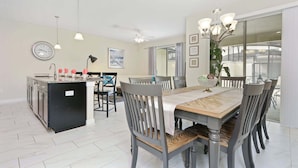 A modern kitchen with a central island, dining table with chairs, and a large window. - Wonderful 4Bd With Pool At Storey Lake Resort 4819 (Kissimmee)